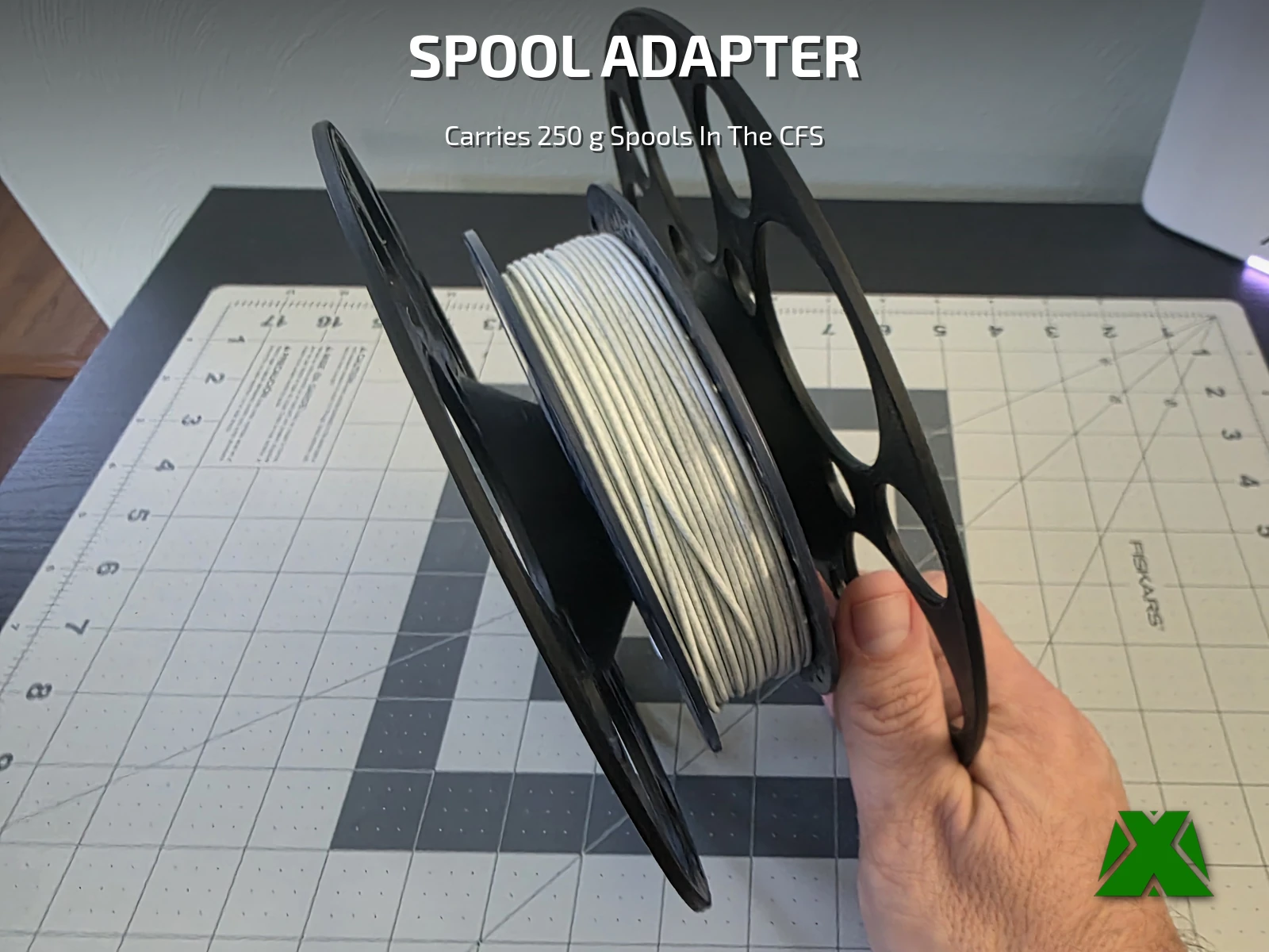 A hand holding the assembled adapter, a white 250 g spool captured between its two spoked flanges