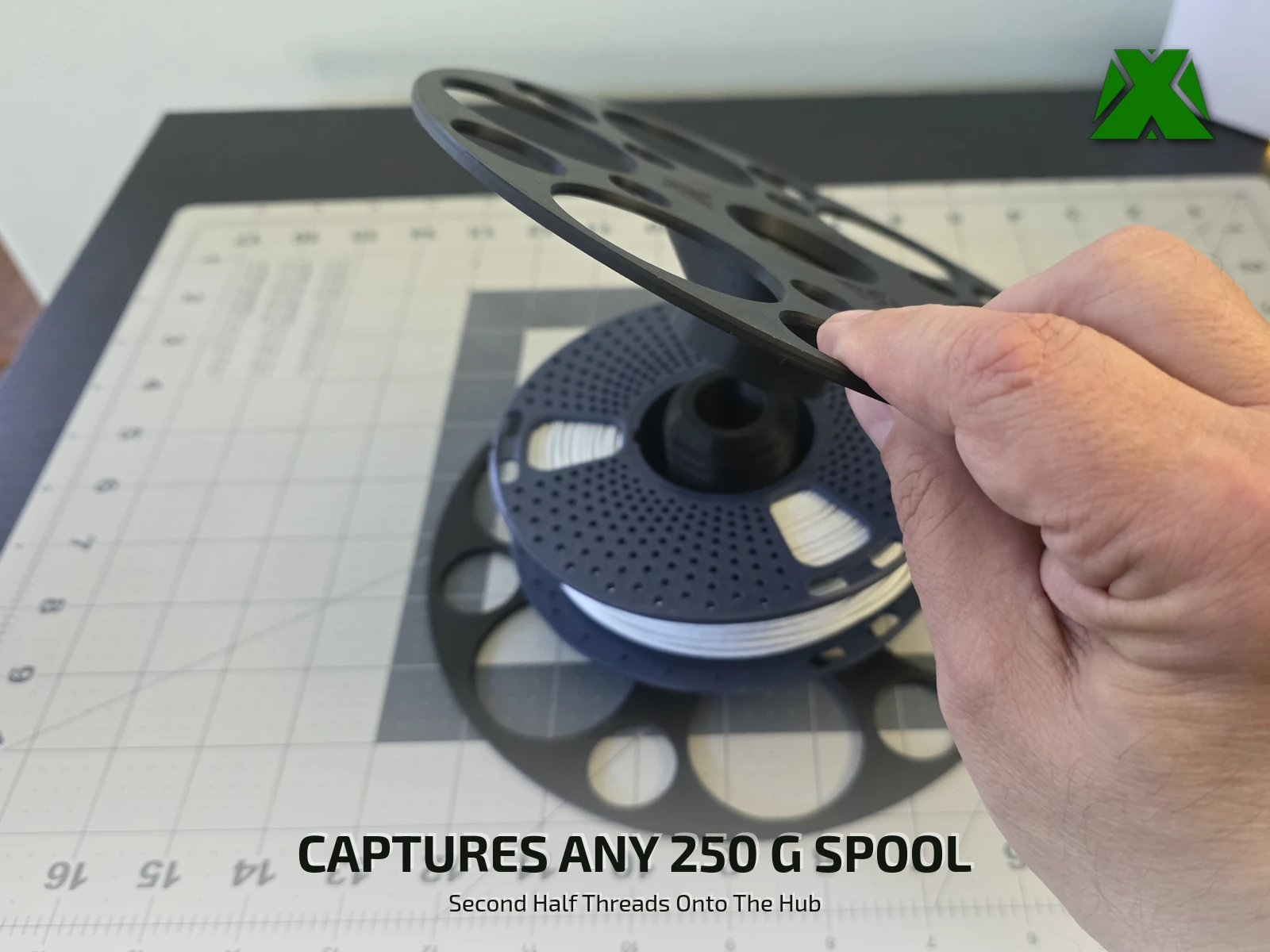 A hand lowering the second flange onto the threaded hub standing up through a navy 250 g spool