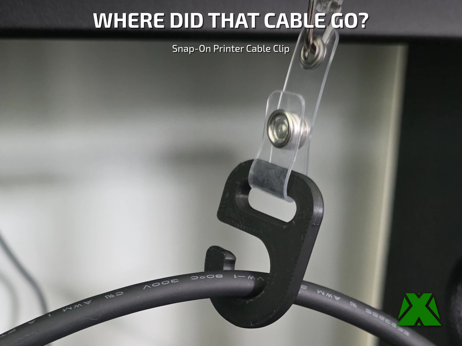 The black printed hook snapped over a printer cable, with the clear strap of a retractable badge reel threaded through its upper loop