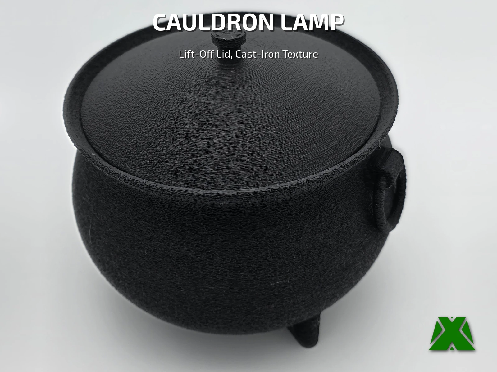 A black cauldron printed with a rough cast-iron texture, lid on, standing on three feet against a pale backdrop