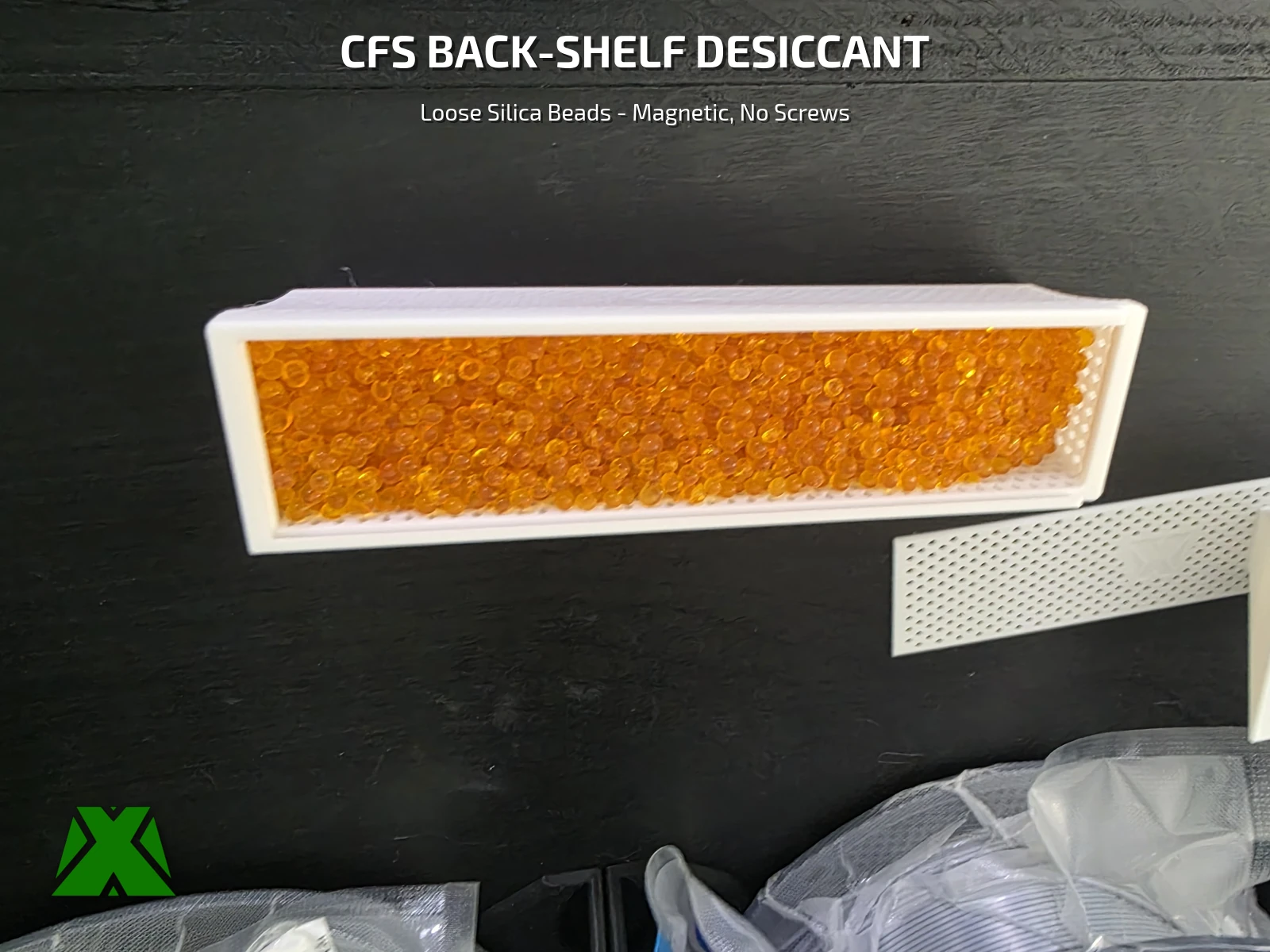 A printed tray filled with orange silica beads, its perforated mesh lid lying alongside