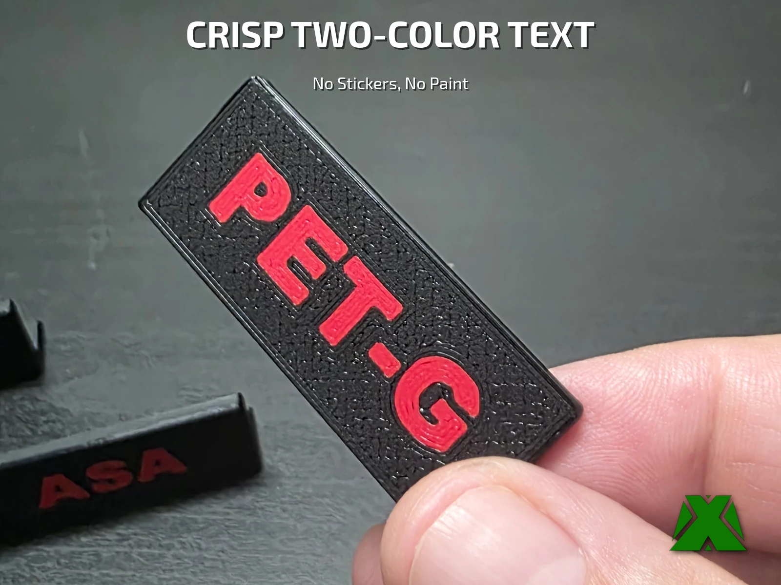 A PET-G label held close to the camera, showing crisp red lettering raised off the textured black body