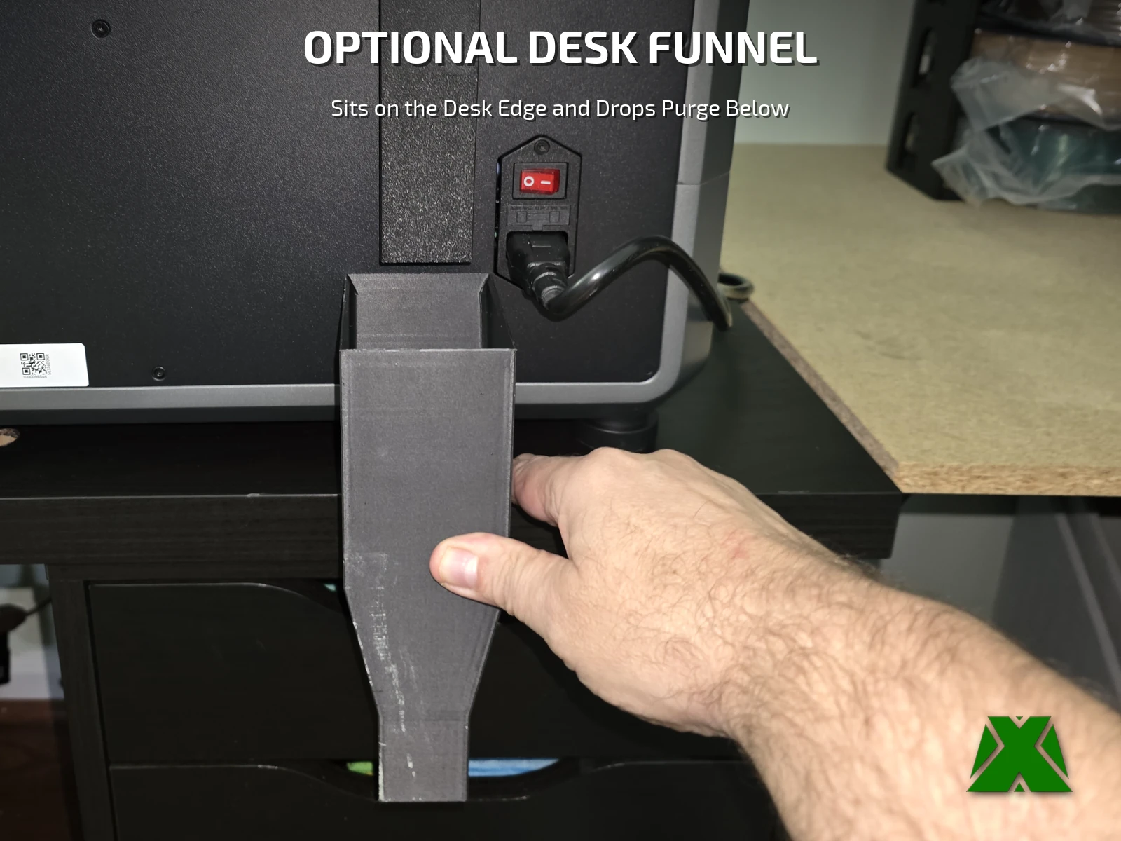 A hand holding the desk funnel on the desk edge directly under the end of the chute, beside the power cord