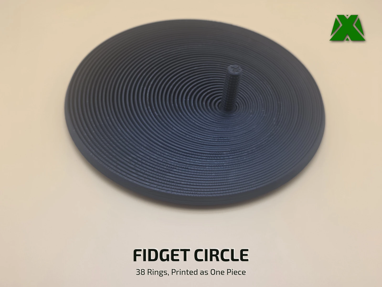 A black print-in-place fidget circle lying flat on a tan backdrop, its 38 concentric rings stepping out from a short textured stem at the center