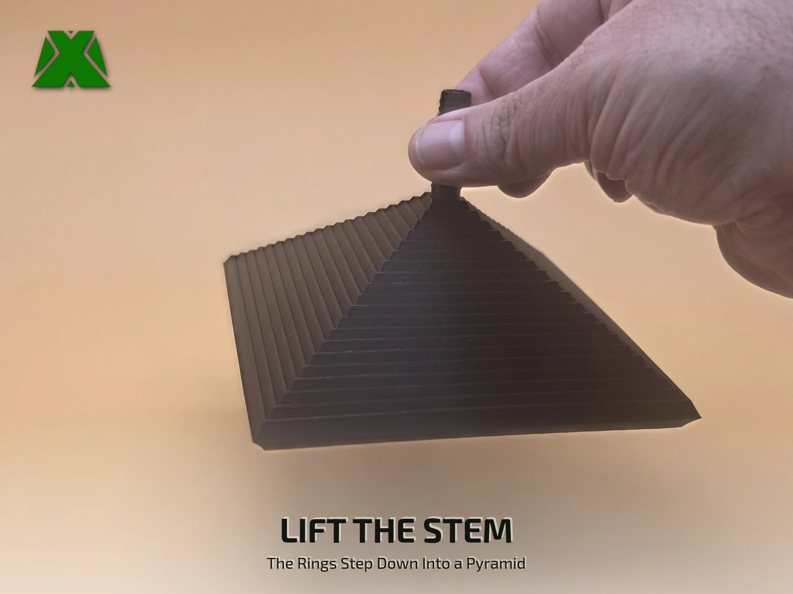 Fingers lifting the fidget square by its textured stem, the 19 rings stepping down below into a four-sided pyramid