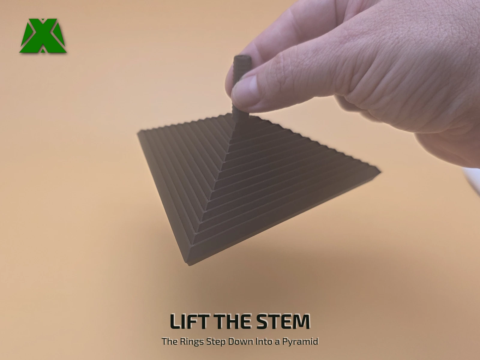 Fingers lifting the fidget triangle by its textured stem, the 13 rings stepping down below into a three-sided pyramid