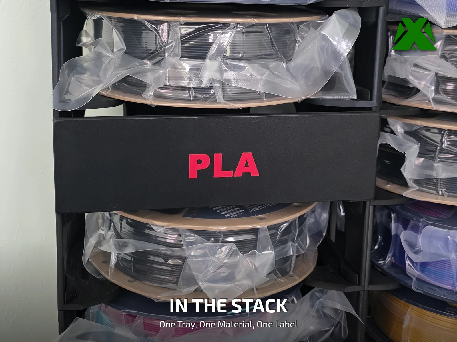A red-on-black PLA insert label standing in a loaded tray in front of its spool