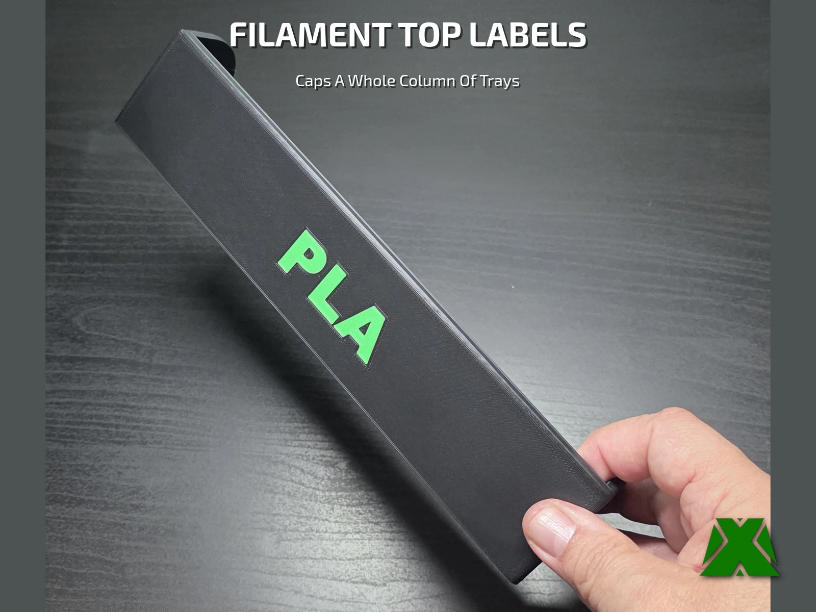 A long black top-label bar with large green PLA lettering, held in one hand