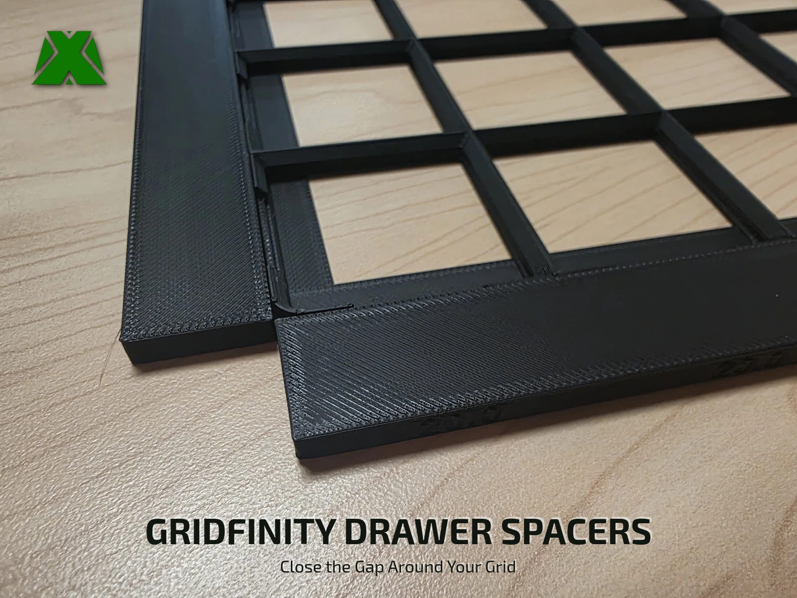 The corner of a black Gridfinity baseplate on a wooden desk with a printed spacer strip fitted along each of its two edges