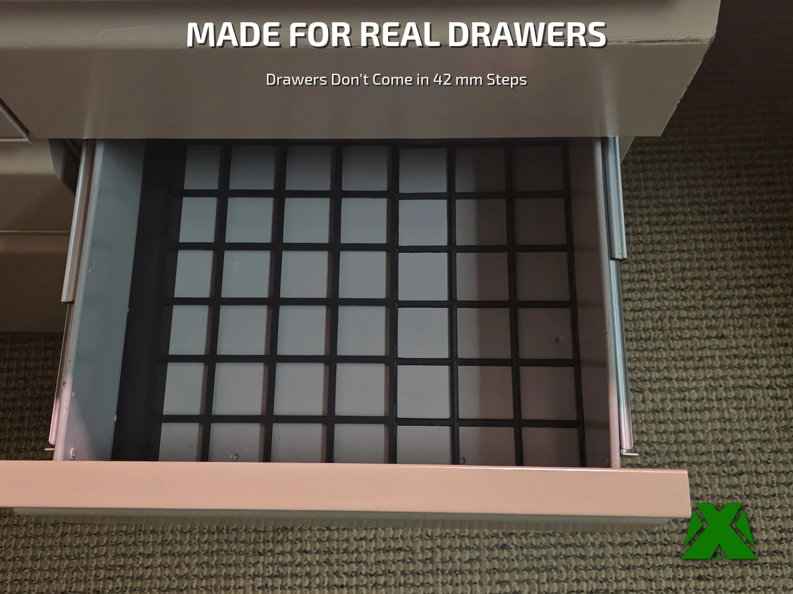An open metal desk drawer with a black Gridfinity baseplate grid filling it wall to wall