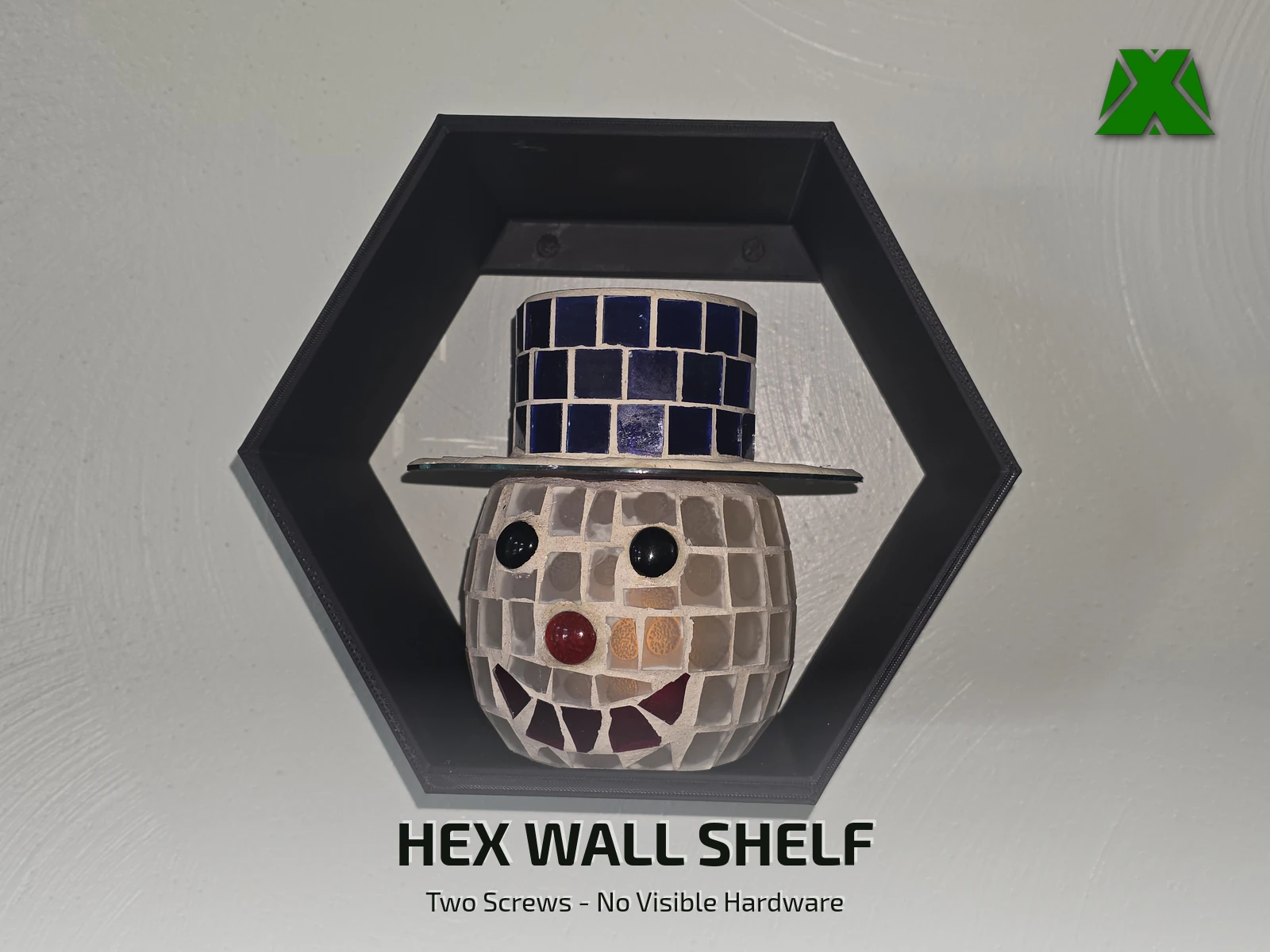 A black hexagonal shelf mounted on a white wall, holding a mosaic snowman candle holder in a blue tile top hat
