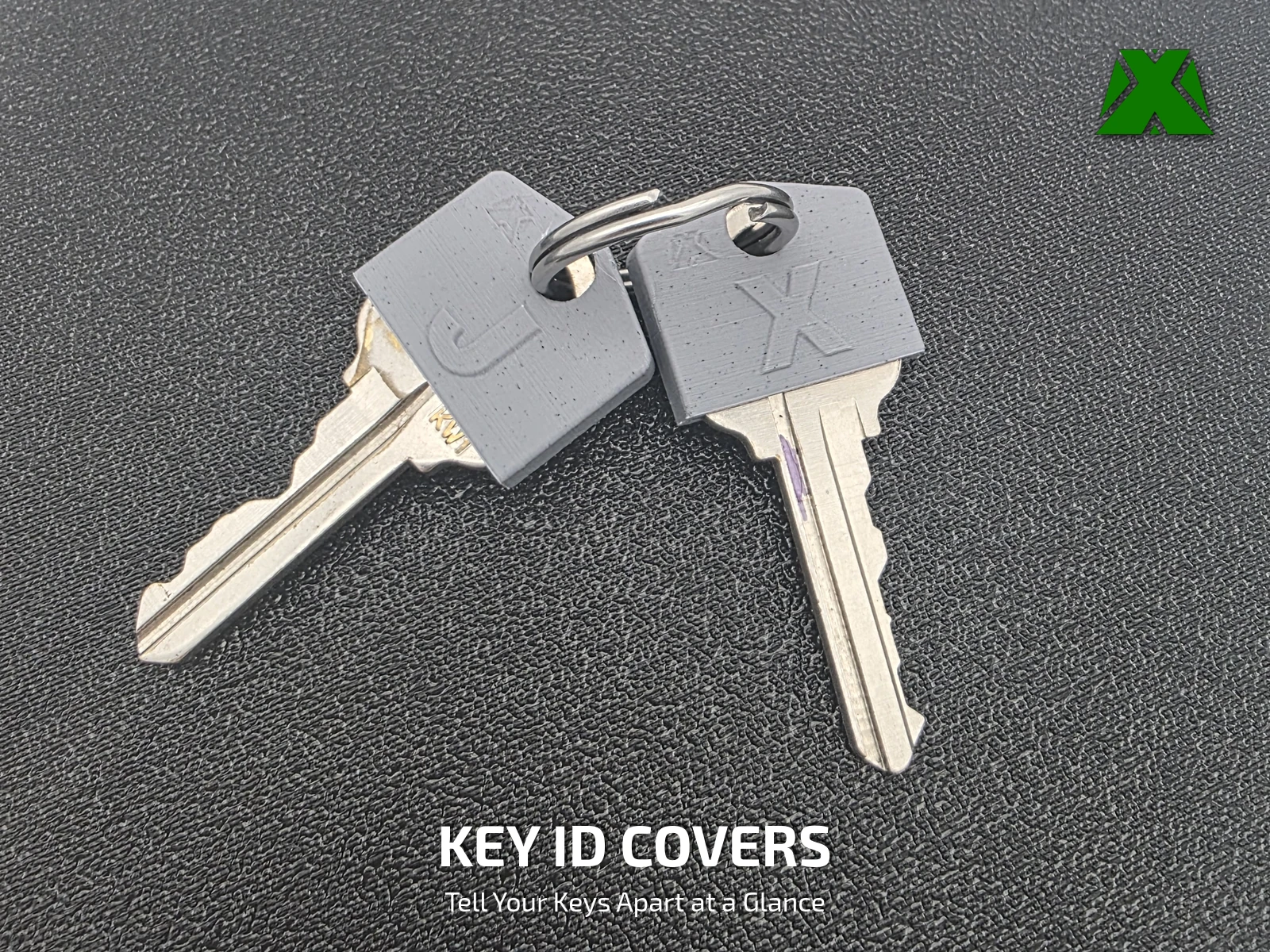 Two brass keys on a split ring, each wearing a gray printed cover with a raised J and X