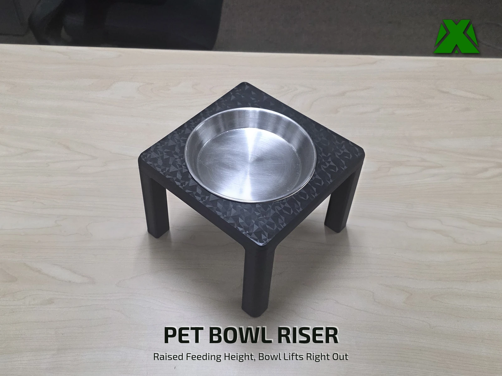 The riser printed in black on a light wood table, holding a stainless steel pet bowl at raised feeding height