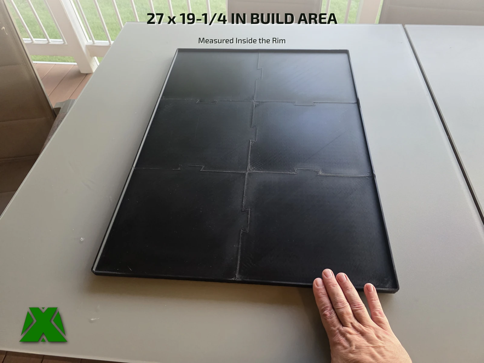 A hand resting on the near corner of the assembled tray, giving its size against a patio table