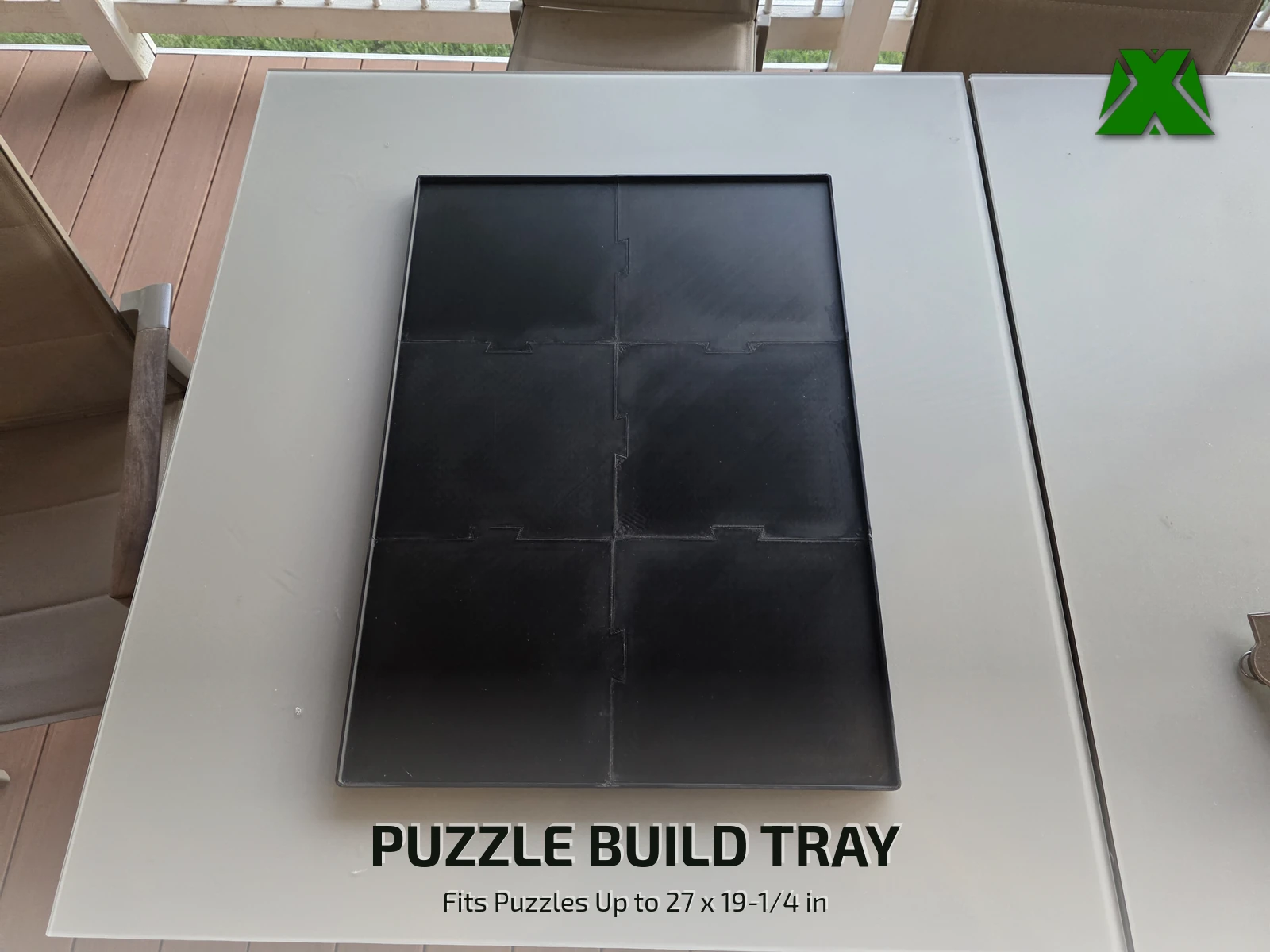 The assembled black puzzle tray on a light gray patio table, its six panels joined by jigsaw-style tabs