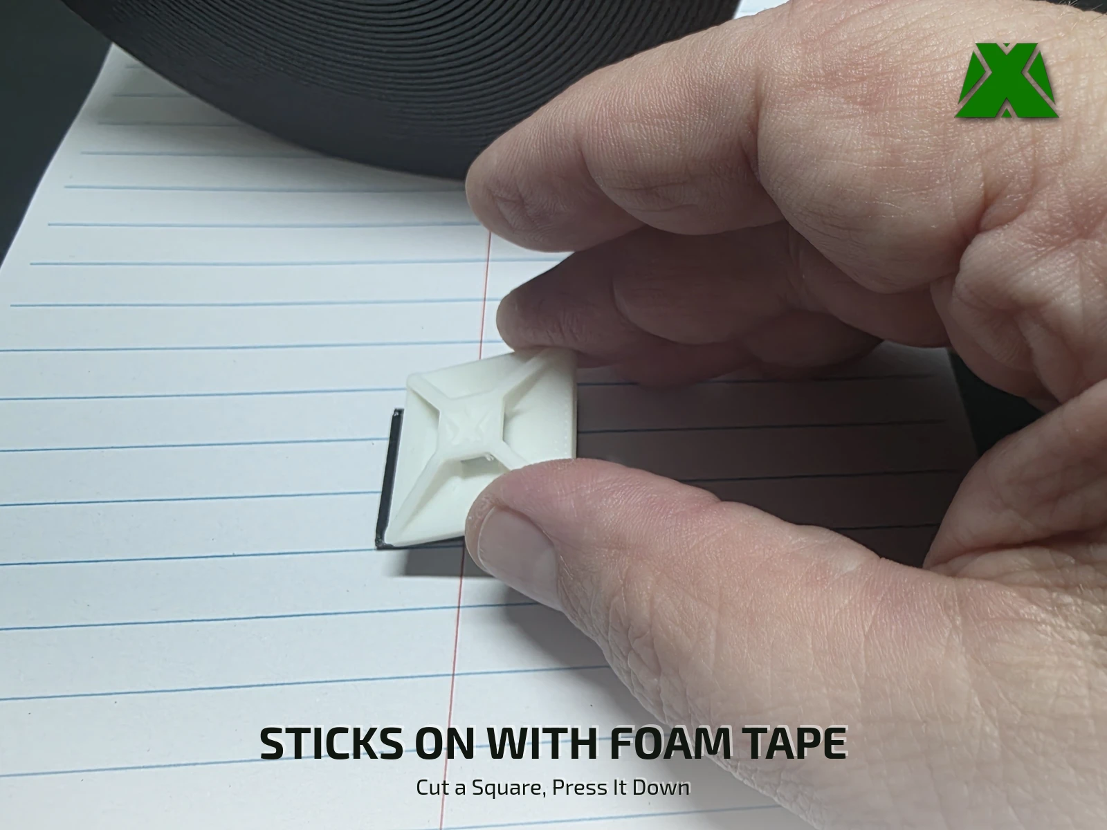 Fingers pressing a square of black foam tape onto the flat underside of a clip